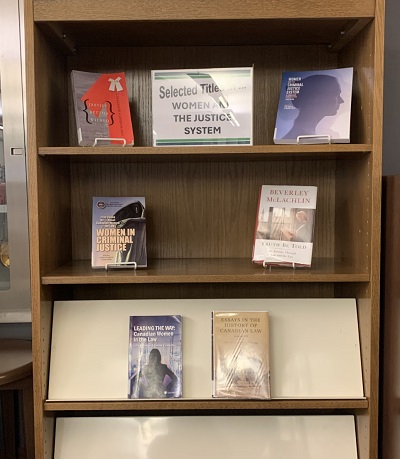 Photo of books on display in the Calgary law library with a sign in front that says "Selected titles in... Women and the Justice System"