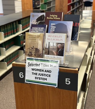 Photo of books on display in the Edmonton law library with a sign in front that says "Selected titles in... Women and the Justice System"